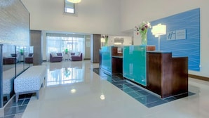 A modern hotel lobby with a reception desk, seating area, and a large window providing natural light.