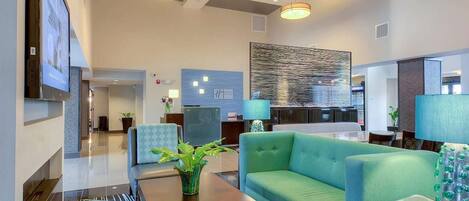 A spacious lobby with a green sofa, a wooden coffee table, and a large abstract wall art piece.