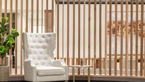 Un sillón blanco con patas de madera, una mesita redonda y una planta en una cesta de mimbre.
