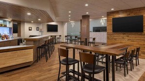 Un restaurante moderno con barra, distintas opciones de asientos y una pantalla grande en la pared.