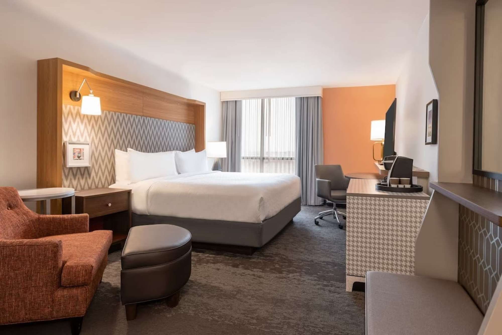 Hotellihuone, jossa on suuri sänky, työpöytä tuolilla, sohva ja pieni jalkarahi.