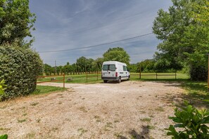 Een witte bus geparkeerd op een grindpad, omringd door groen en een houten hek.