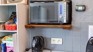 Una cocina con un microondas sobre una estantería de madera, una tetera y varios alimentos en la encimera.