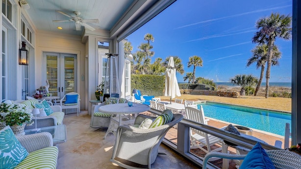 A balcony with a pool, wicker furniture, and palm trees. - Amazing Oceanfront estate (Hilton Head)