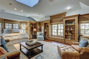 A spacious bedroom with a large bed, a sitting area with a sofa and armchair, built-in wooden bookshelves, and a skylight. - Amazing Oceanfront estate (Hilton Head)