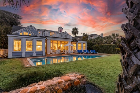 A large house with a swimming pool, a patio with chairs, and a stone wall. - Amazing Oceanfront estate (Hilton Head)