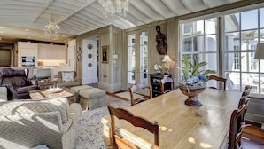A spacious living room with a large wooden dining table, comfortable seating, and a view through large windows. - Amazing Oceanfront estate (Hilton Head)