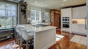 A kitchen with a central island, wooden cabinets, and a view through large windows. - Amazing Oceanfront estate (Hilton Head)