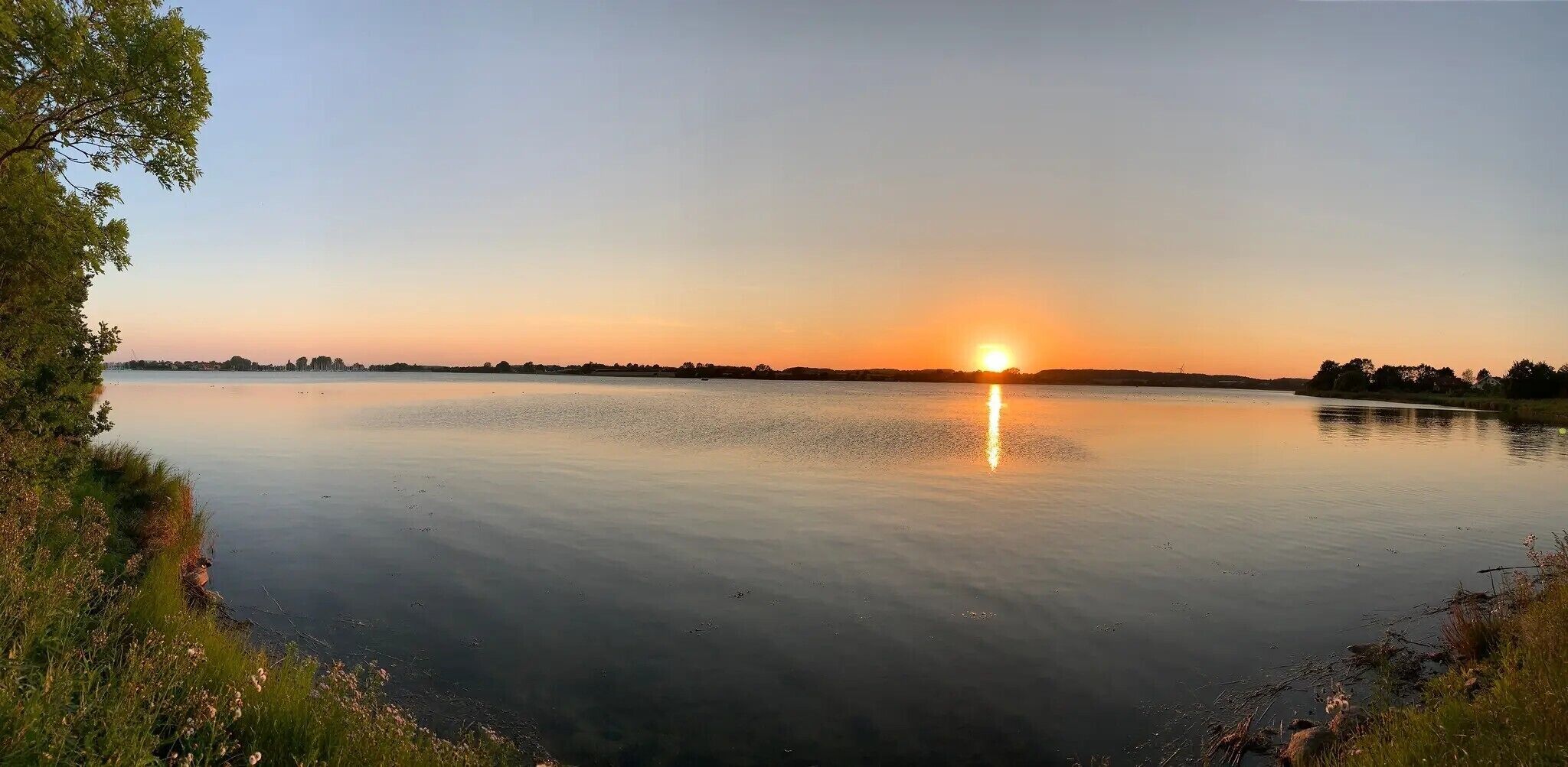 Un lac paisible au coucher du soleil, sous un ciel dégagé.