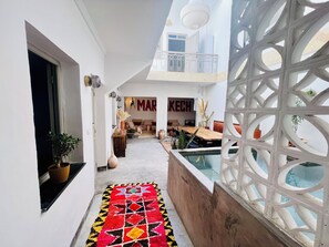 Un corridoio stretto con un tappeto colorato, una zona piscina con un divisorio in reticolo bianco e una sala da pranzo con il cartello 'MARKECH'.