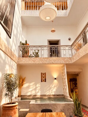 A multi-level interior with a pool area, potted plants, and a balcony with a railing. - Private Family-Run Riad • basin • patio (Marrakech)