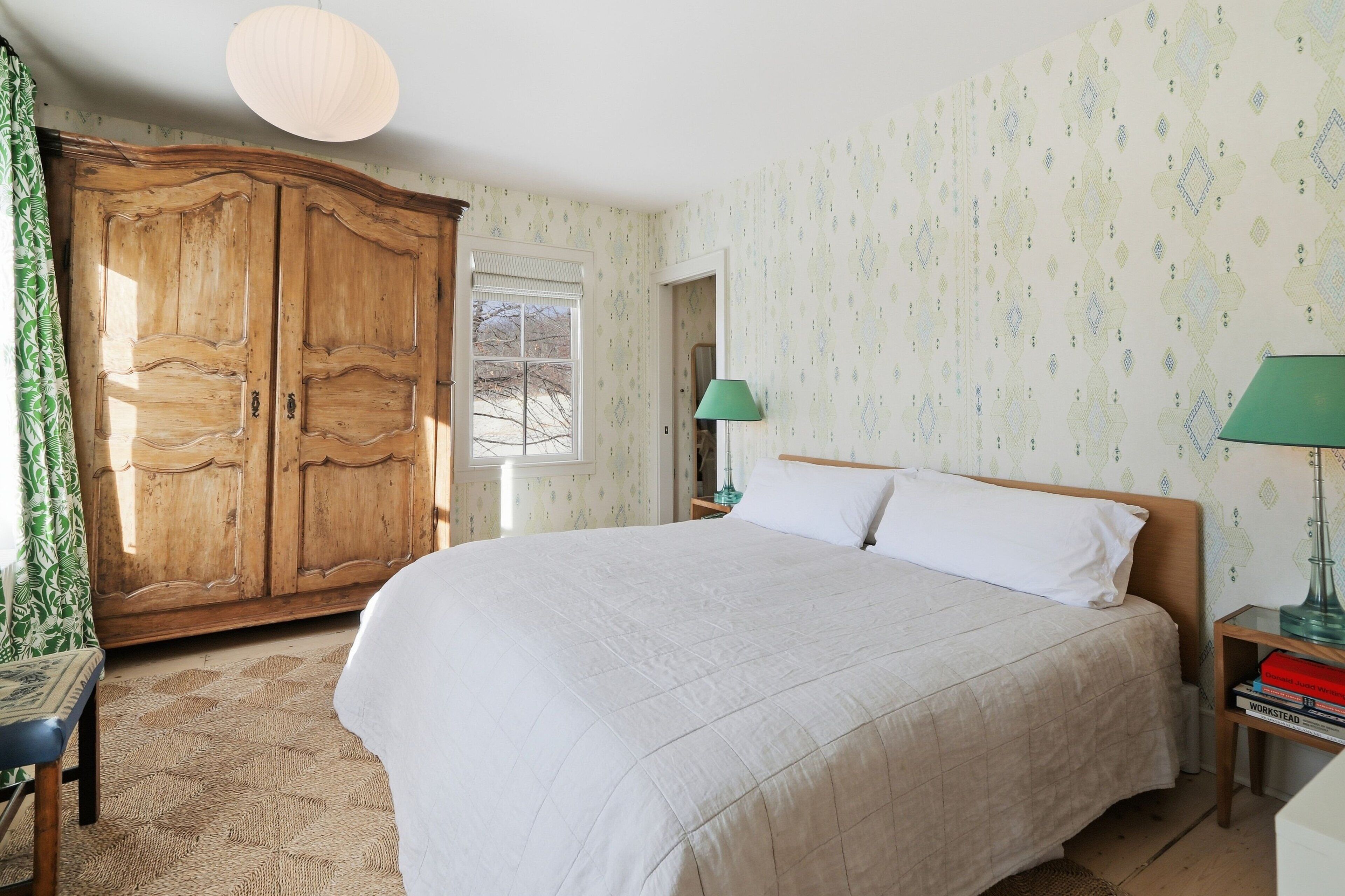 A bedroom with a large bed, wooden wardrobe, and patterned wallpaper.