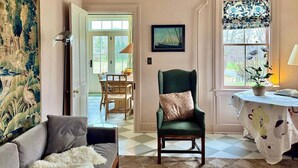 A living room with a green armchair, a sofa, a patterned rug, and a dining area visible through an open door. - Gorgeous Hudson Valley Farmhouse On 14 Acres 3 Bedroom Home (Old Chatham)