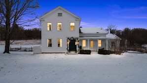A two-story white house with a snow-covered yard and a clear sky. - Gorgeous Hudson Valley Farmhouse On 14 Acres 3 Bedroom Home (Old Chatham)