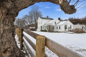 Et træhegn og et snedækket landskab med et hvidt hus i baggrunden.
