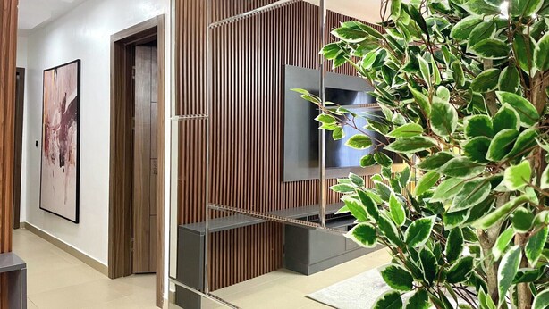 A modern hallway with a wooden panel wall, a mounted TV, and a potted plant. - Holbeck  Apartment  (Abuja)