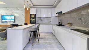 A modern kitchen with white cabinets, a marble backsplash, and a built-in island with bar stools. - Holbeck  Apartment  (Abuja)