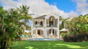 Ein zweistöckiges Haus mit Pool, umgeben von Palmen und einem gepflegten Rasen.