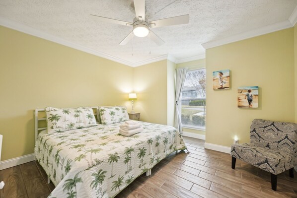 A bedroom with a bed, a chair, a ceiling fan, and artwork on the wall. - Chill by The Shores - Pet Friendly - Fernandina Beach (Fernandina Beach)