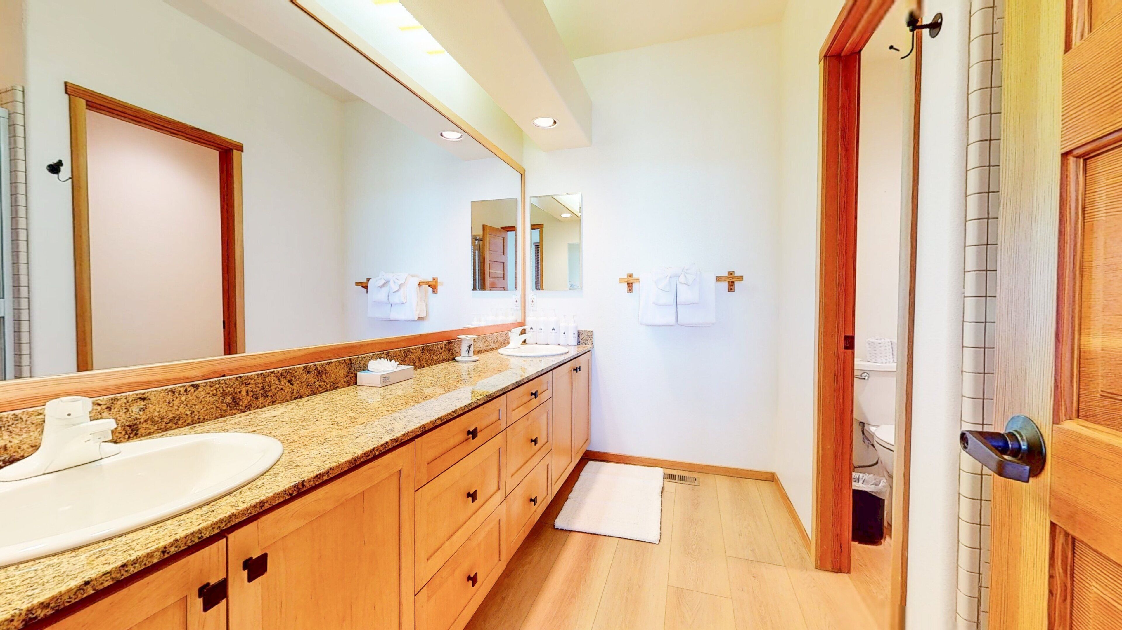 Un baño moderno con dos lavamanos, armarios de madera, un espejo grande y una zona de ducha.