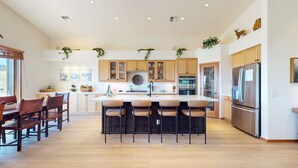 Una cocina moderna con armarios de madera, una isla central con taburetes, un refrigerador y un comedor con sillas.
