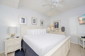 A bedroom with a bed, bedside tables, a ceiling fan, framed artwork, and a window with blinds. - Phoenix V 1411 1 Bedroom Condo (Orange Beach)