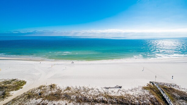 Ein Strand mit klarem Himmel, sandigem Ufer und einer Holzpromenade, die zum Wasser führt.