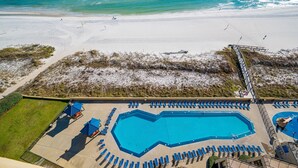 Ein Poolbereich mit blauen Sonnenschirmen, einem großen Pool und Blick auf den Strand.