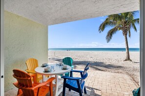 A beachside patio with a table set for two, colorful chairs, and a view of the ocean. - Nautilus #111 2 Bedroom Home (Holmes Beach)