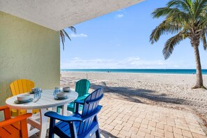 A beachside patio with a table set for two, chairs, and a view of the beach and ocean. - Nautilus #111 2 Bedroom Home (Holmes Beach)