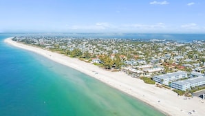 Eine Vogelperspektive einer Küstenstadt mit einem langen Sandstrand, einem dicht bebauten Wohngebiet und einem strahlend blauen Himmel.