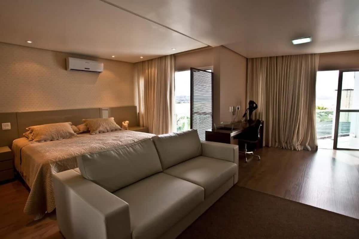 Een moderne hotelkamer met een groot bed, een slaapbank, een bureau en uitzicht op het omliggende landschap.