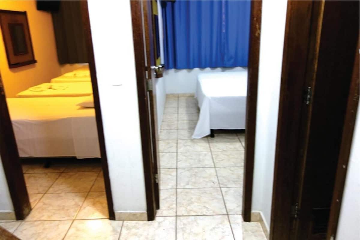 Een smalle gang met een bed aan de linkerkant en een groter bed aan de rechterkant, beide bedekt met witte lakens.
