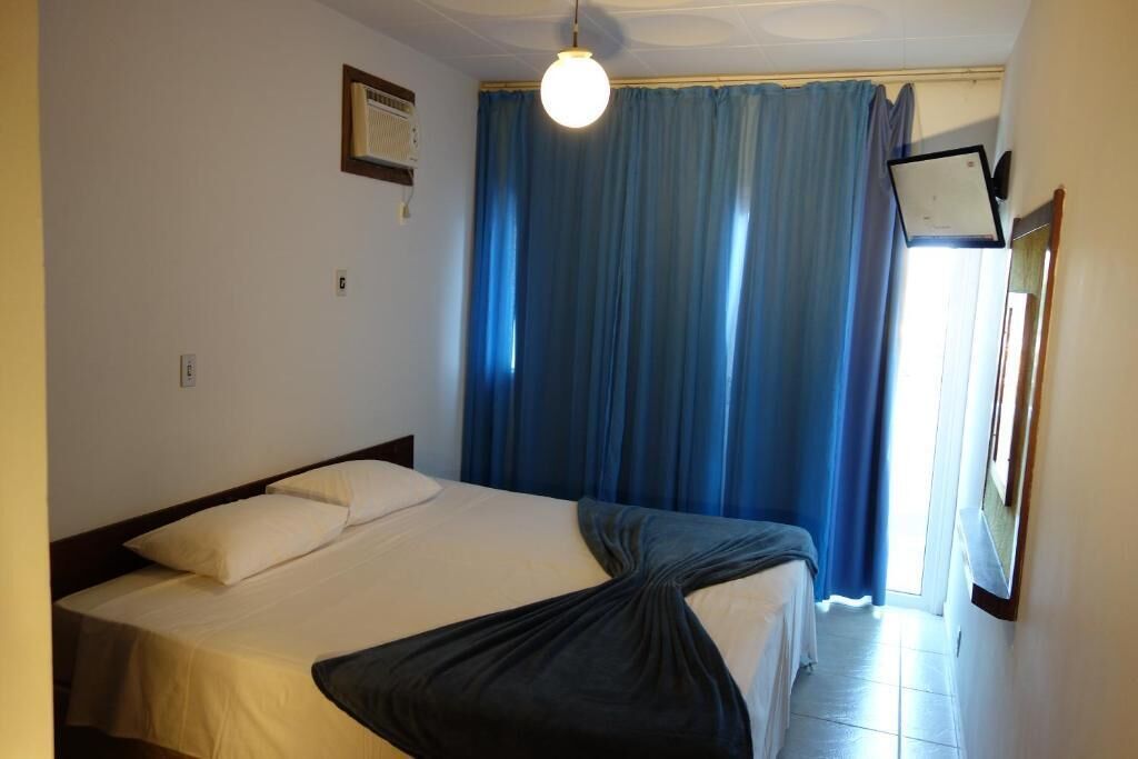 A hotel room with a bed, a ceiling fan, and a window with blue curtains.