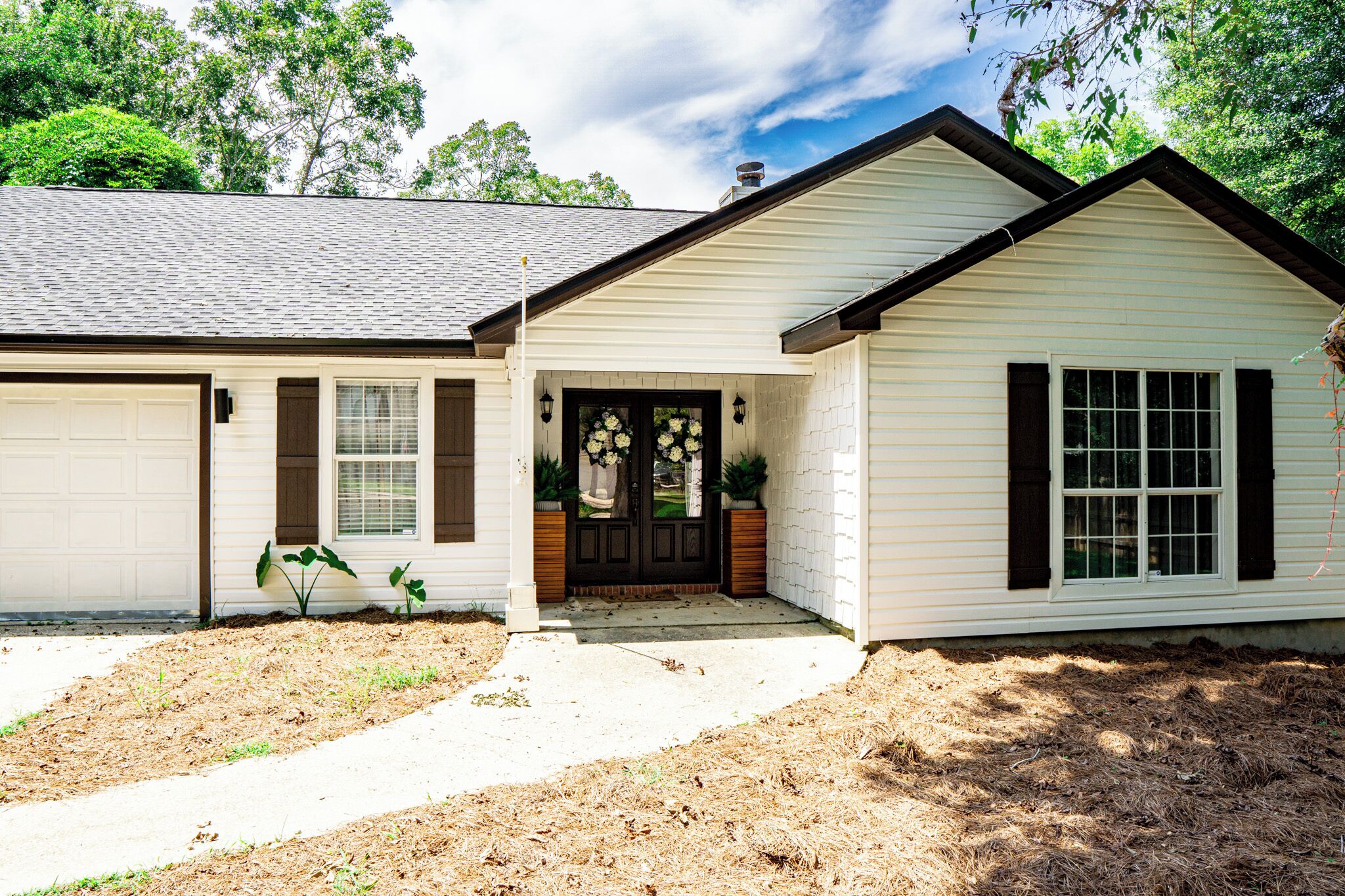 A two-story house with a garage, a front porch with a black door, and a small garden area.