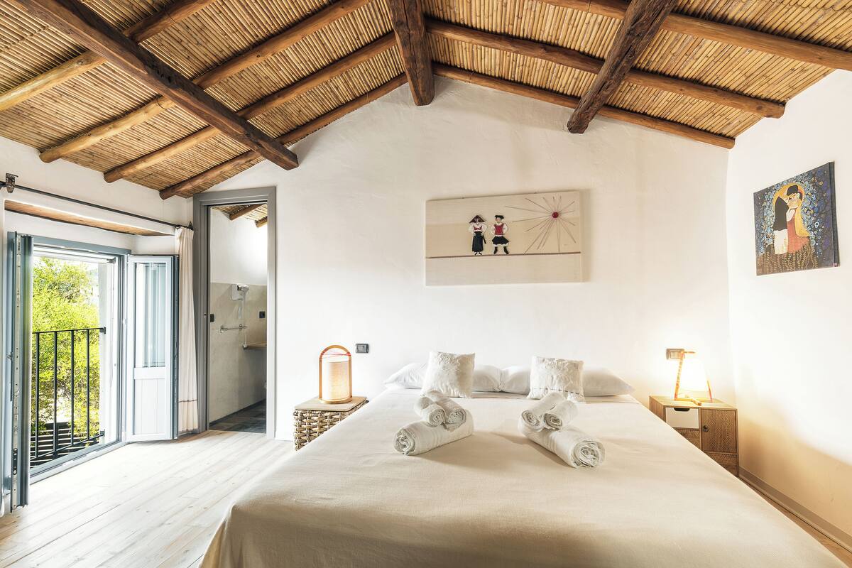Un dormitorio con techo de madera, una cama con toallas dobladas, lámparas de noche y un cuadro en la pared.