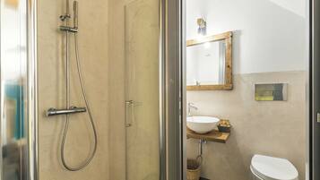 Une salle de bain avec une douche à parois de verre, un lavabo blanc et une étagère en bois.