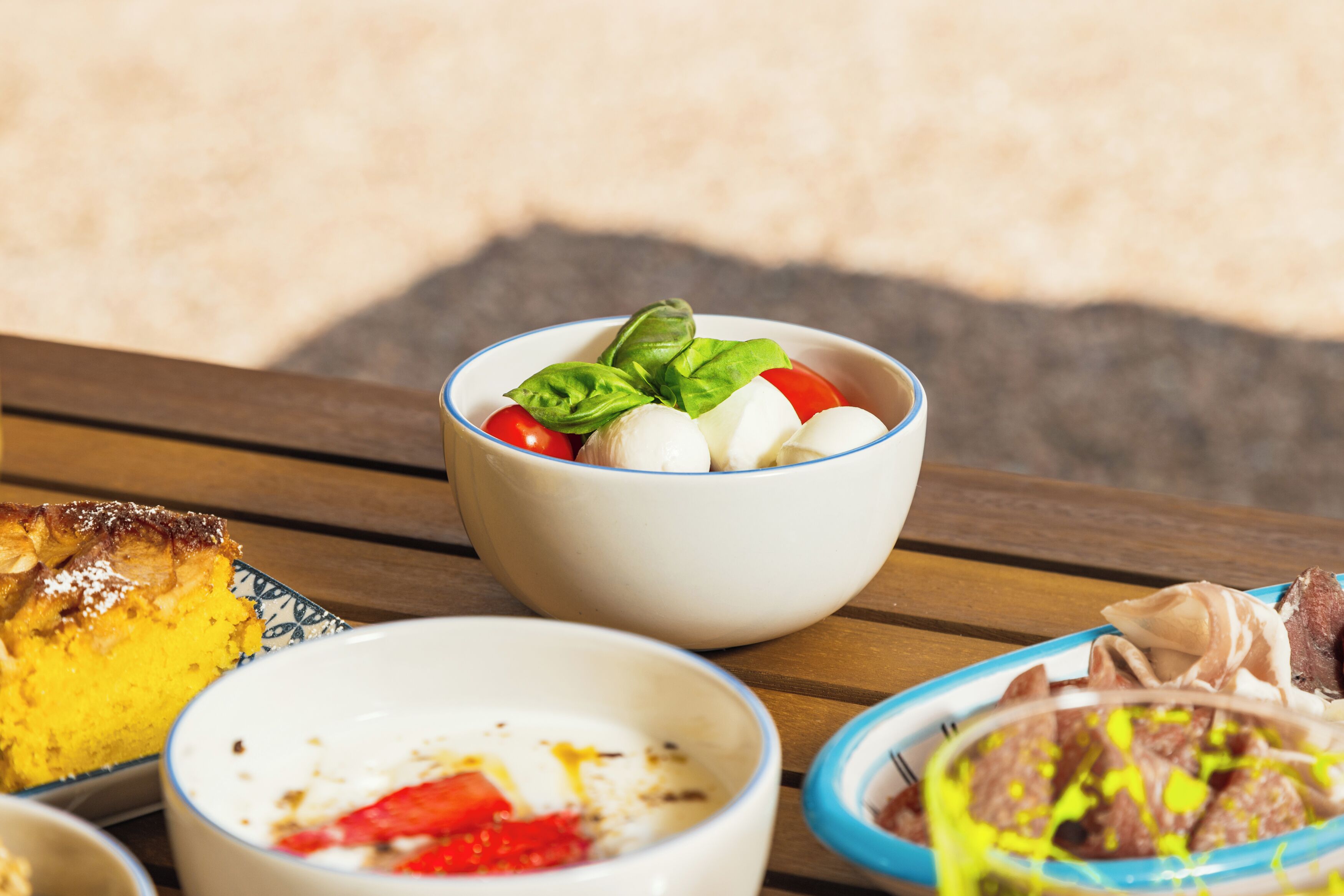 Une table où l’on trouve divers plats, notamment un saladier de salade de tomates et de mozzarella, une part de gâteau, un bol de yaourt aux fruits et un plat de viande et de légumes.