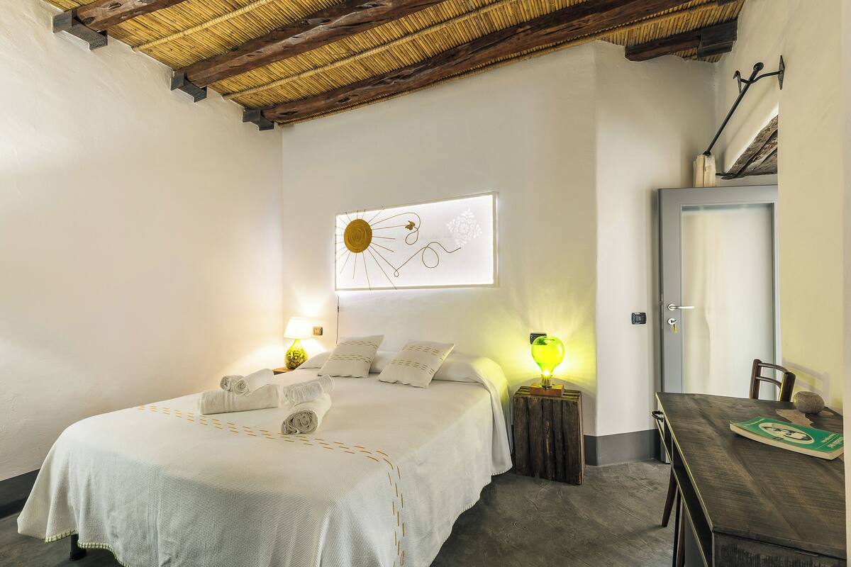 Un dormitorio con cama, lámparas de noche, un cuadro, una mesa de comedor y una puerta.