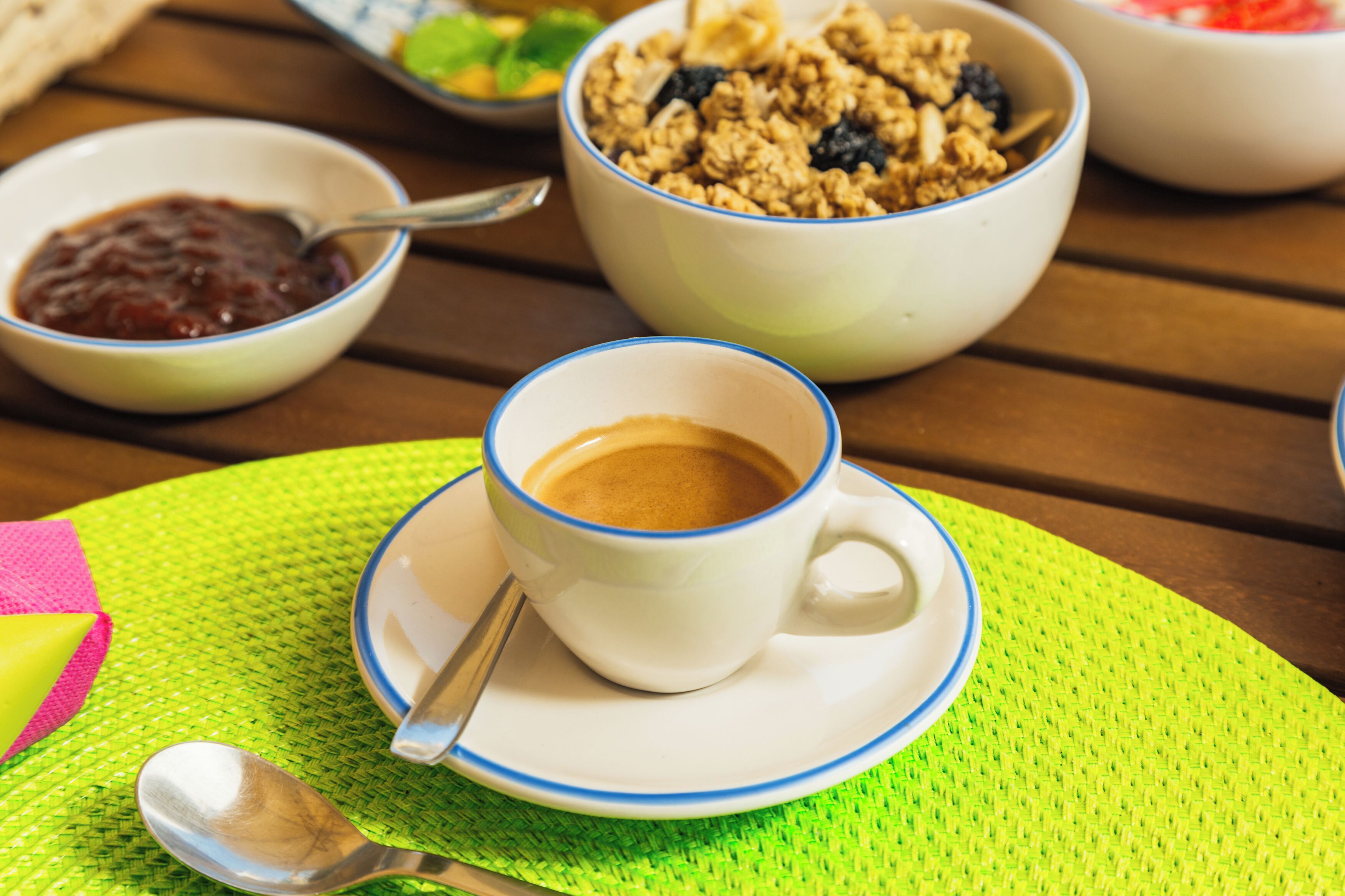 Une table avec une tasse de café, un bol de granola et un bol de confiture.