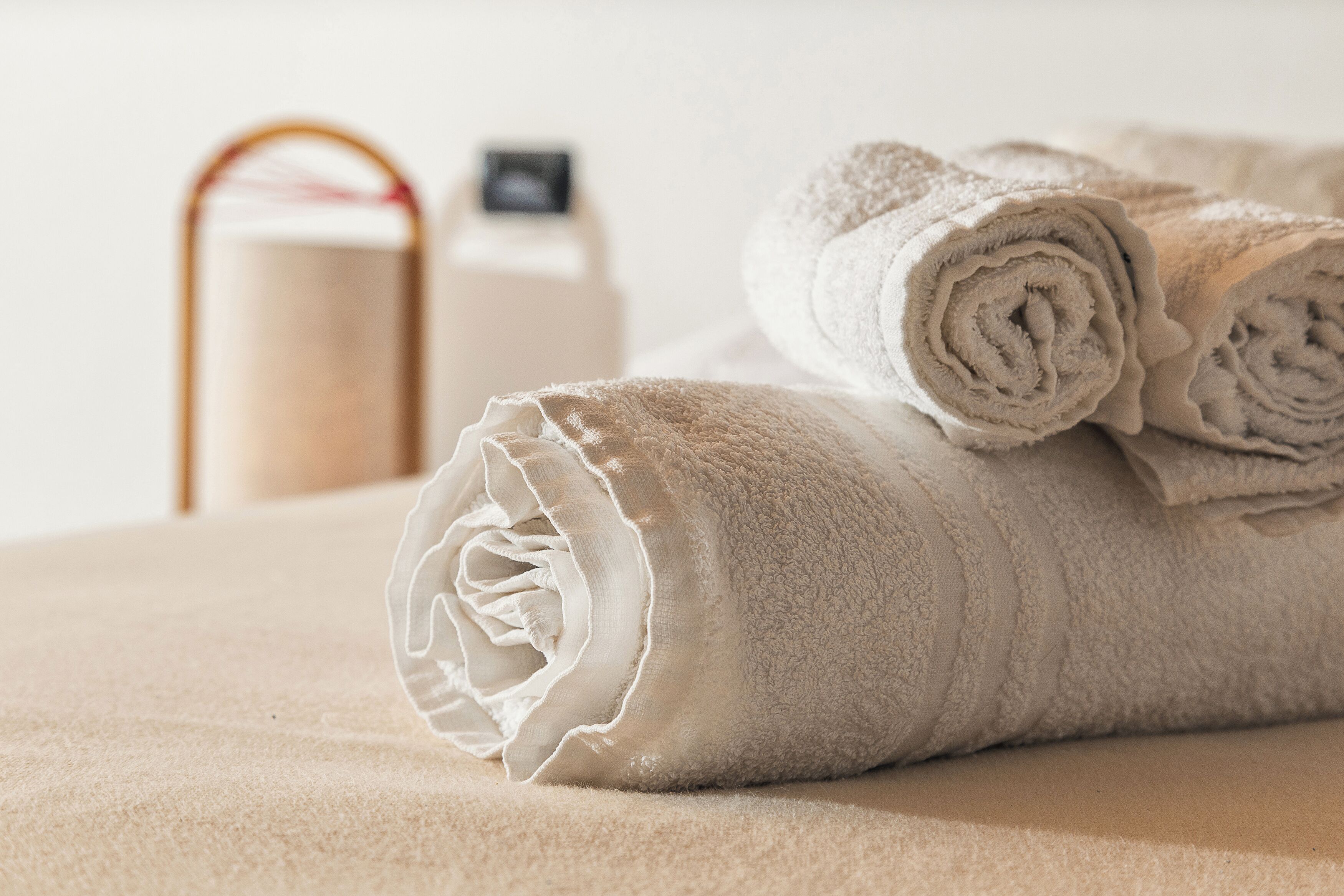 A neatly folded white towel on a beige surface, a bottle of lotion, and a toiletry bag in the background.