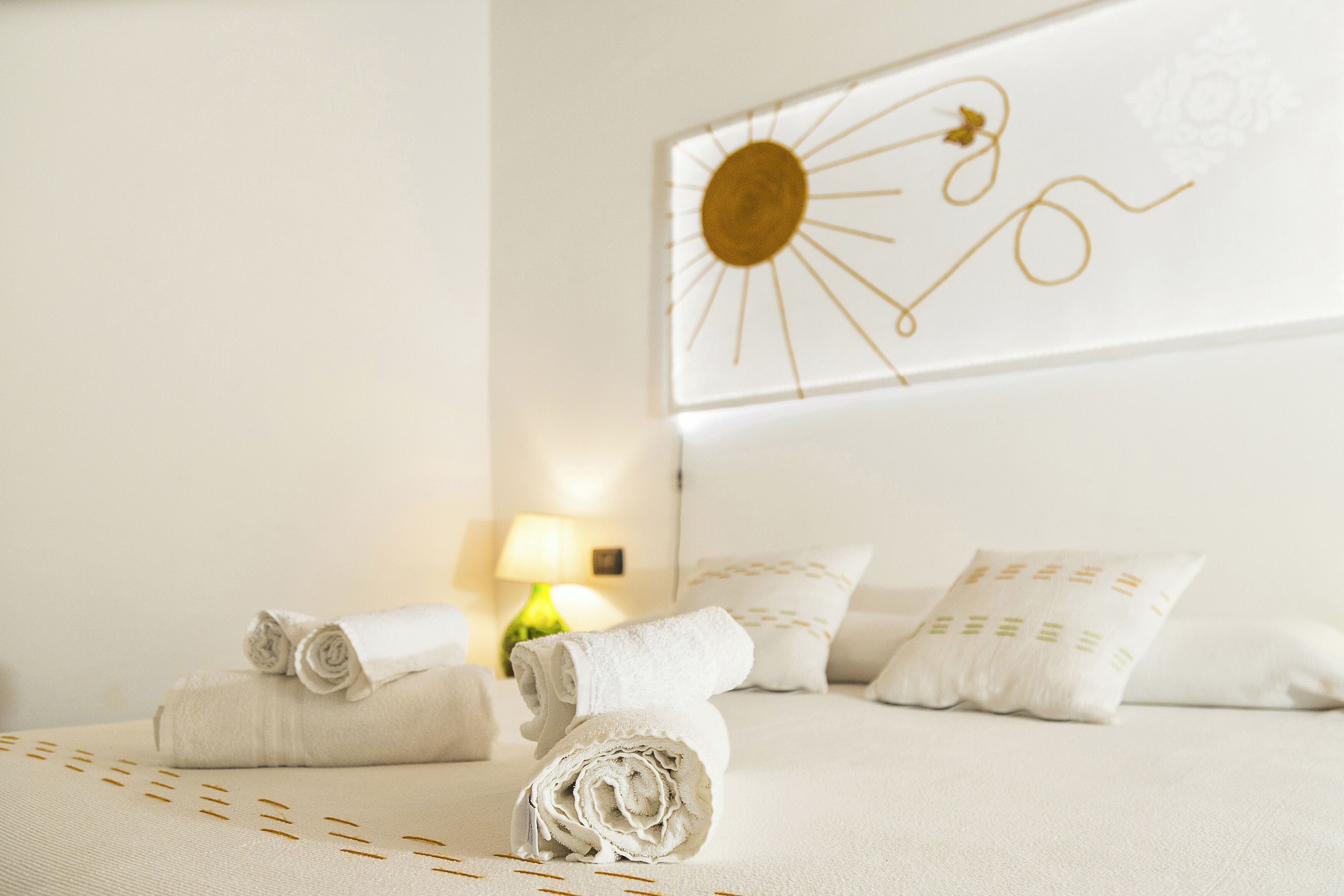 Una cama bien hecha con toallas enrolladas y almohadas, un reloj de pared y una lámpara al fondo.
