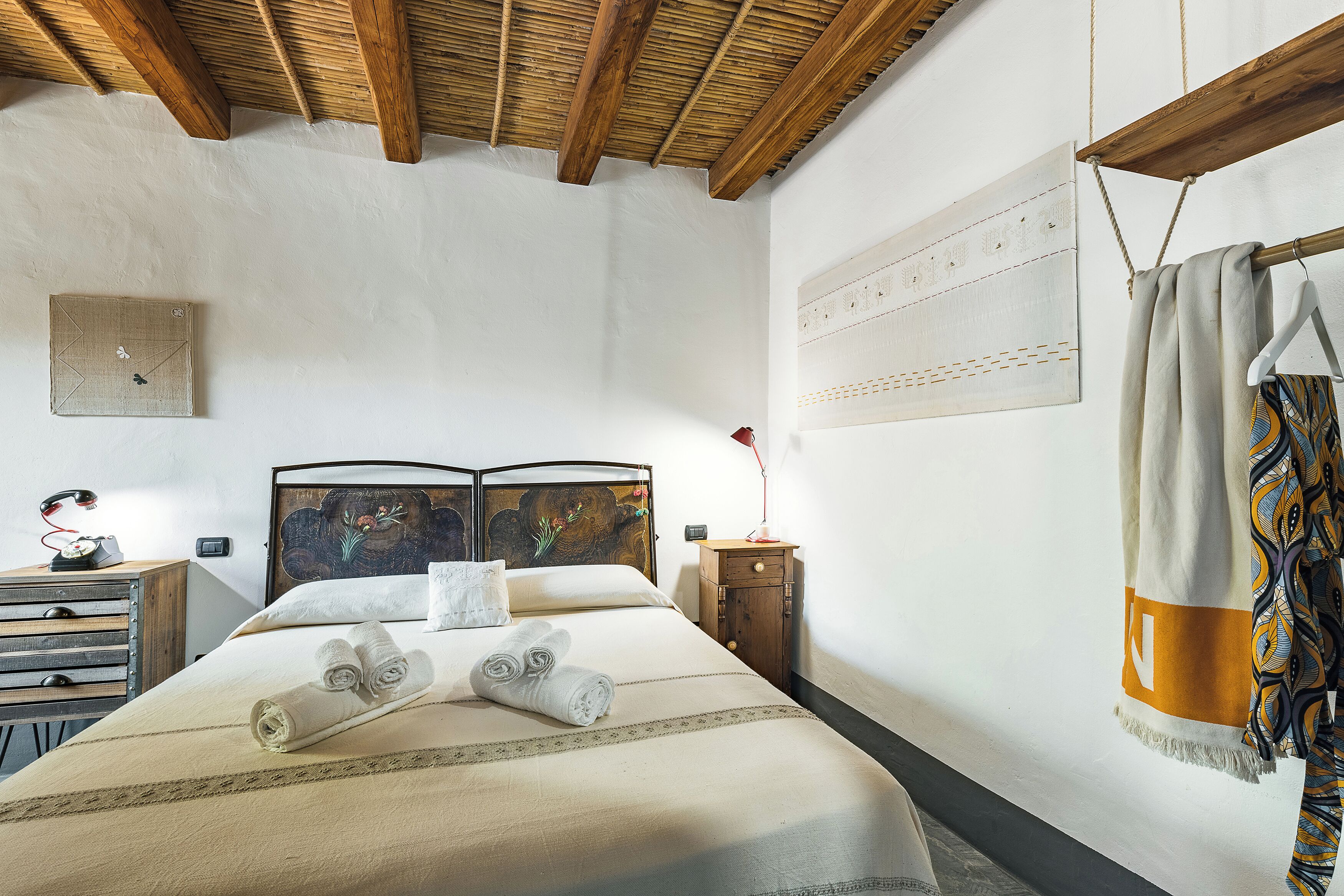 Un lit bien fait, avec des serviettes pliées, une tête de lit en bois, une table de chevet avec une lampe et une œuvre d’art accrochée au mur.