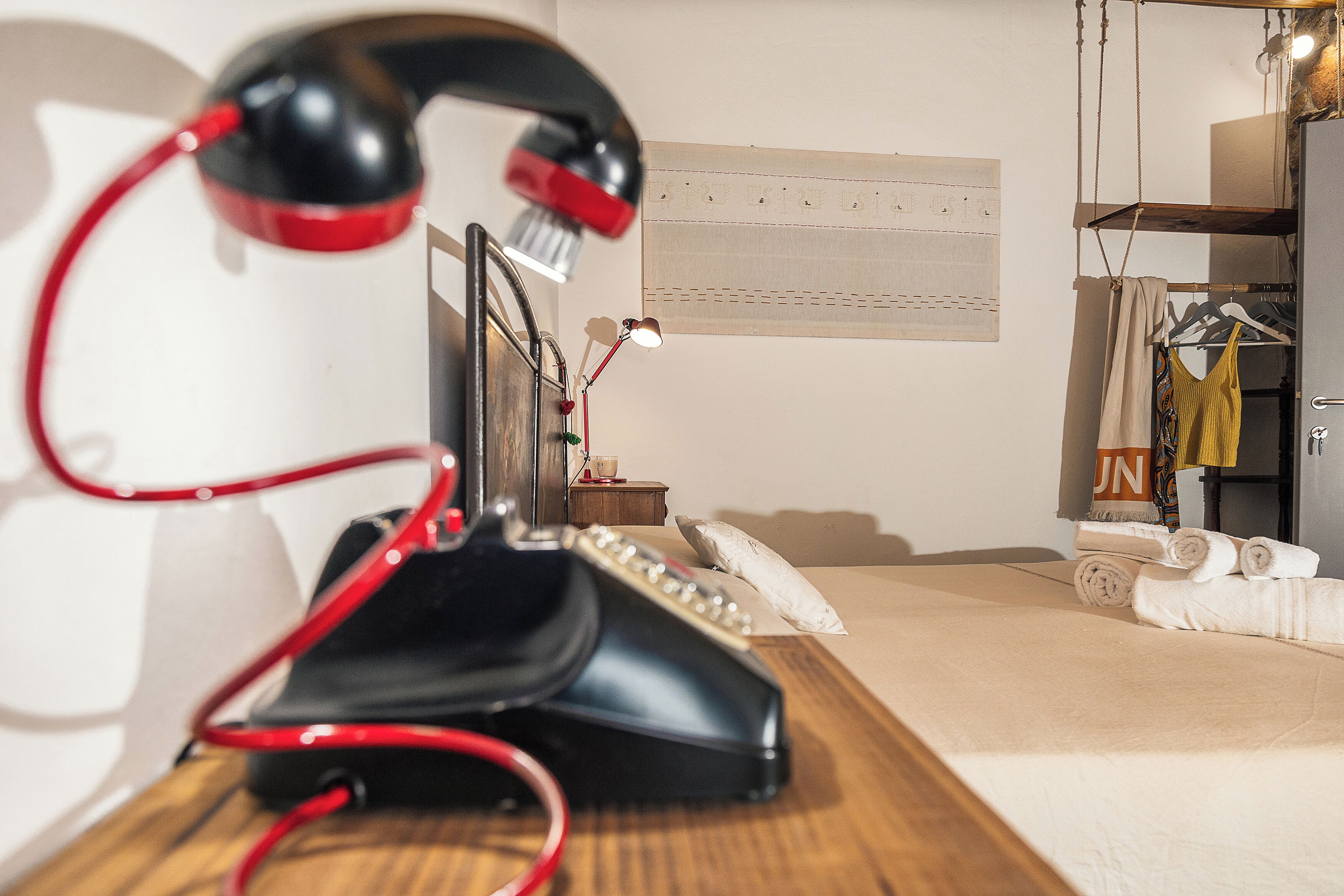 A hotel room with a bed, a desk with a telephone, a lamp, and a clothing rack with towels.