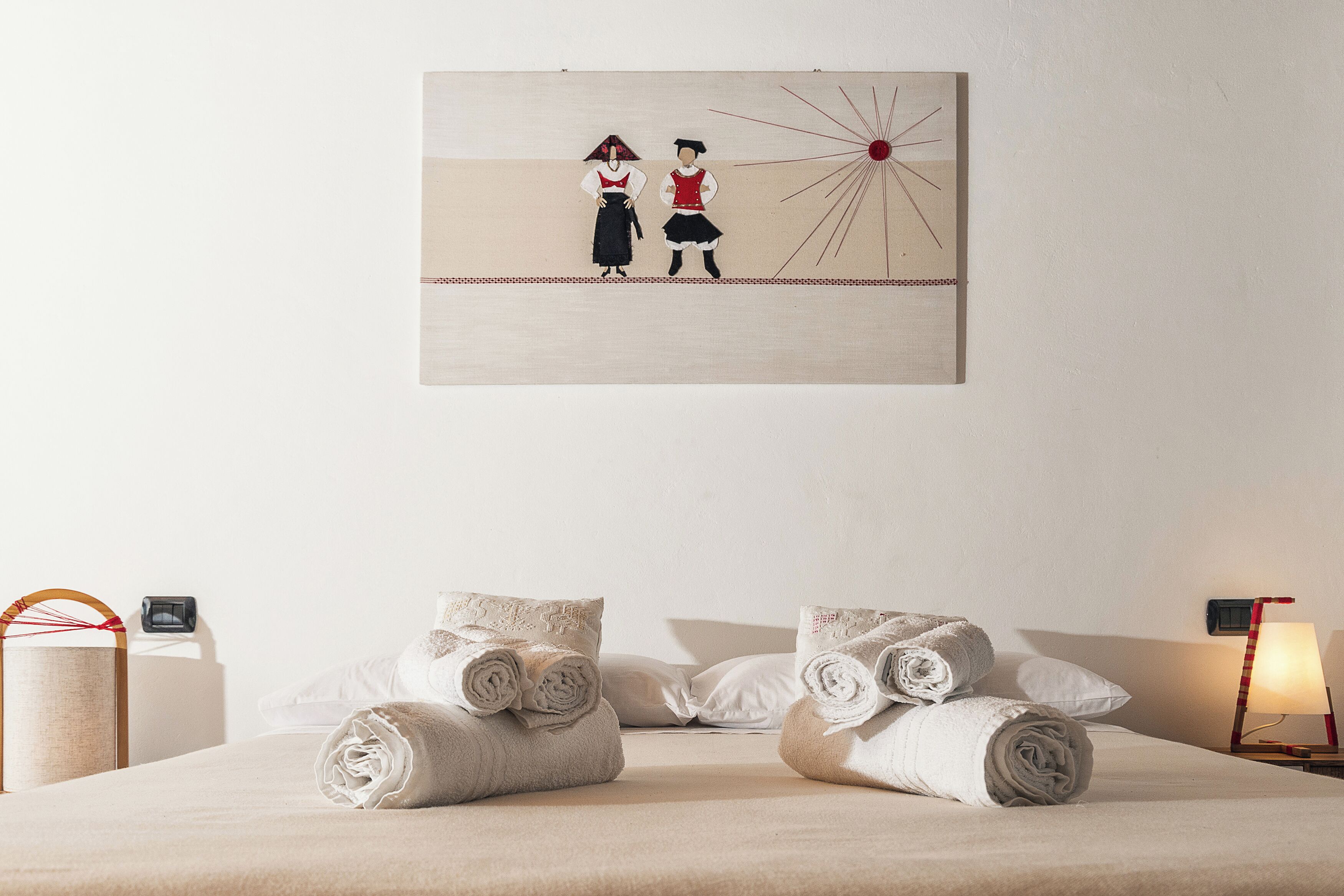 Habitación de hotel con una cama, almohadas y una obra de arte en la pared que representa dos figuras.