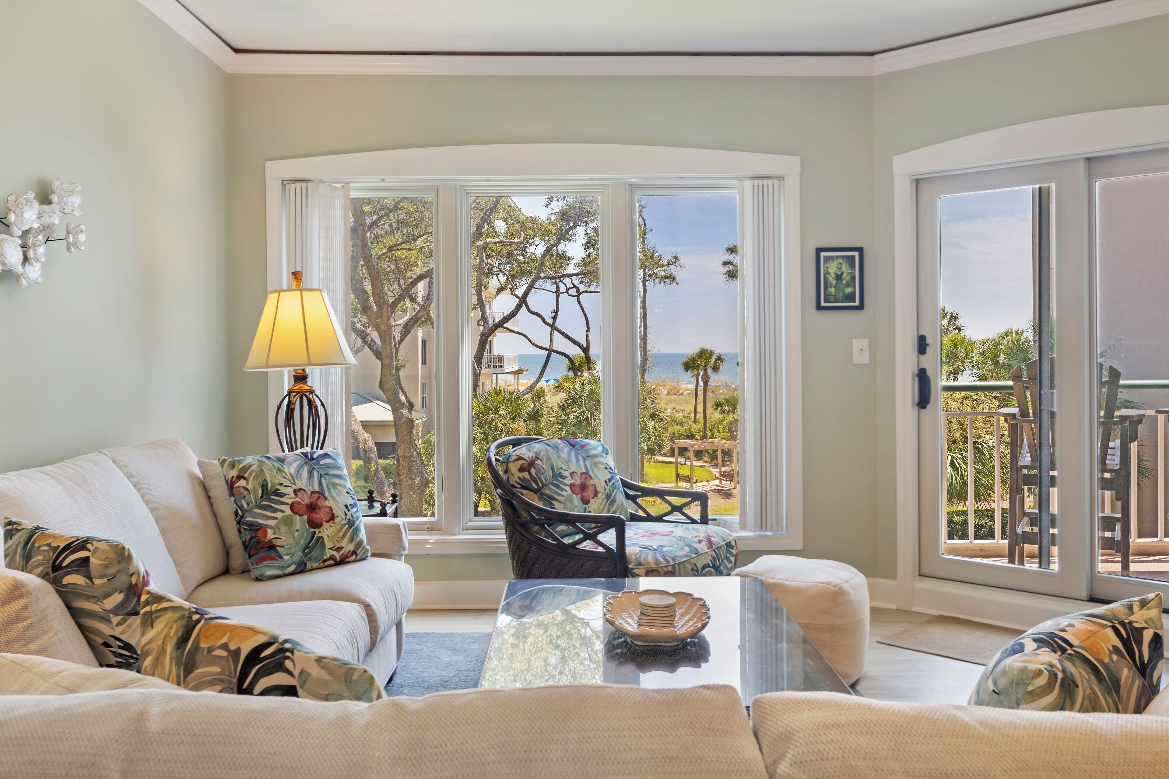 A living room with a sofa, a chair, a table, and a view of the sea through large glass doors.