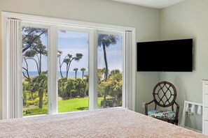 A bedroom with a large window, a bed, a chair, and a flat-screen TV mounted on the wall. - Stunning 2 Bedroom Villa with sweeping views of the Atlantic (Hilton Head Island)