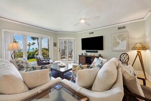 A spacious living room with a large TV, comfortable seating, a ceiling fan, and a view of the outdoors. - Stunning 2 Bedroom Villa with sweeping views of the Atlantic (Hilton Head Island)