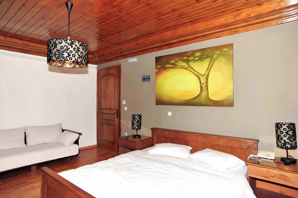 Cozy bedroom with warm wooden details, featuring a comfortable double bed and a sofa bed, soft lighting, and a relaxing atmosphere—perfect for unwinding after exploring Lake Doxa and the Goura mountains.