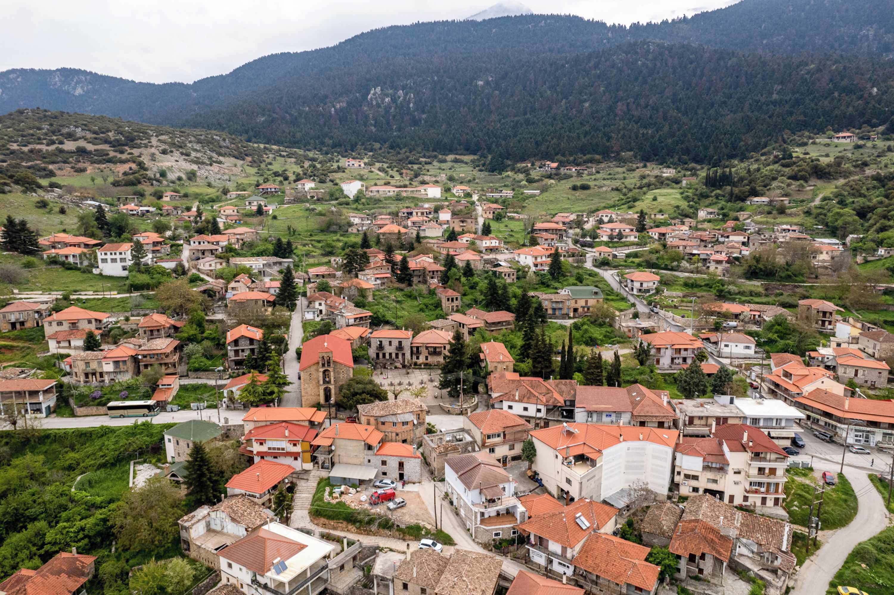 Un poble amb edificis de teulades vermelles, una església al centre i una muntanya de fons.